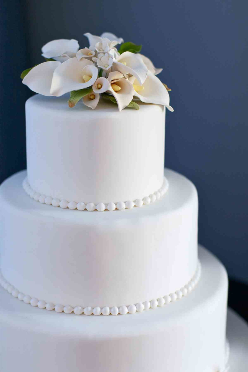 Simple tiered white wedding cake with pearls and lilies